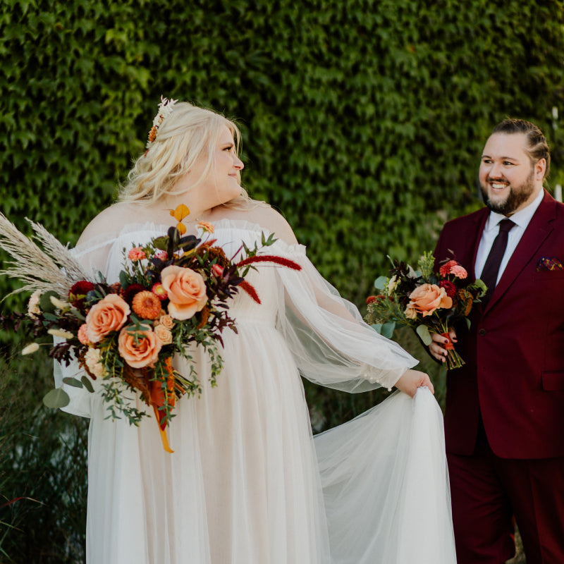 A bride holding a flower bouquet showing off her dress to her bridesman