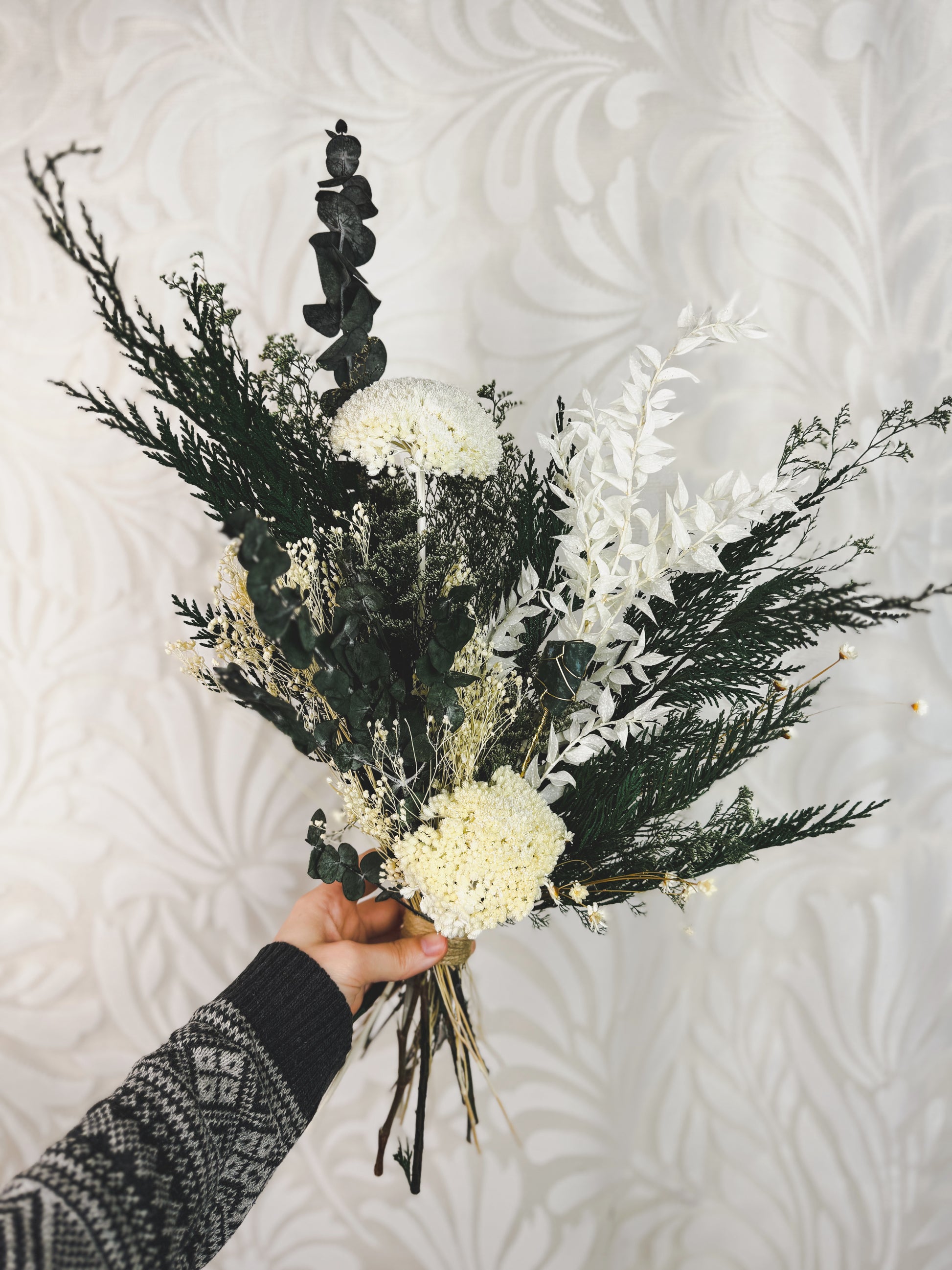 Dried flower bouquet featuring preserved cedar and other green and white ingredients.