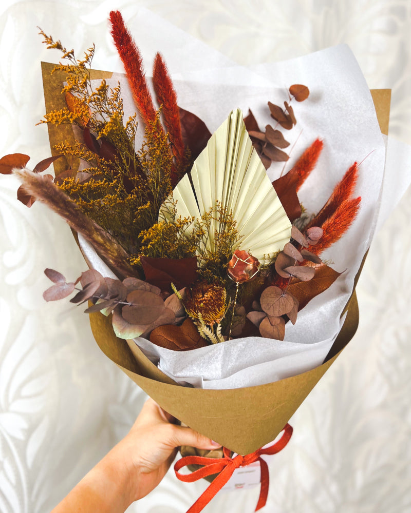 A bouquet of orange, rust, and mustard dried flowers with a Raw Carnelian crystal in the center