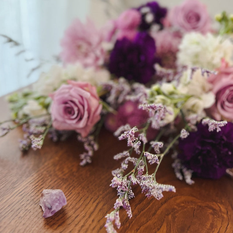 A fresh flower bouquet laying on its side in a purple color palette inspired by the amethyst crystal sitting next to it.
