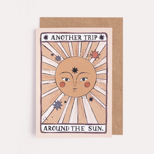 A tarot-inspired greeting card with a picture of the sun smiling that says "Another Trip Around the Sun"