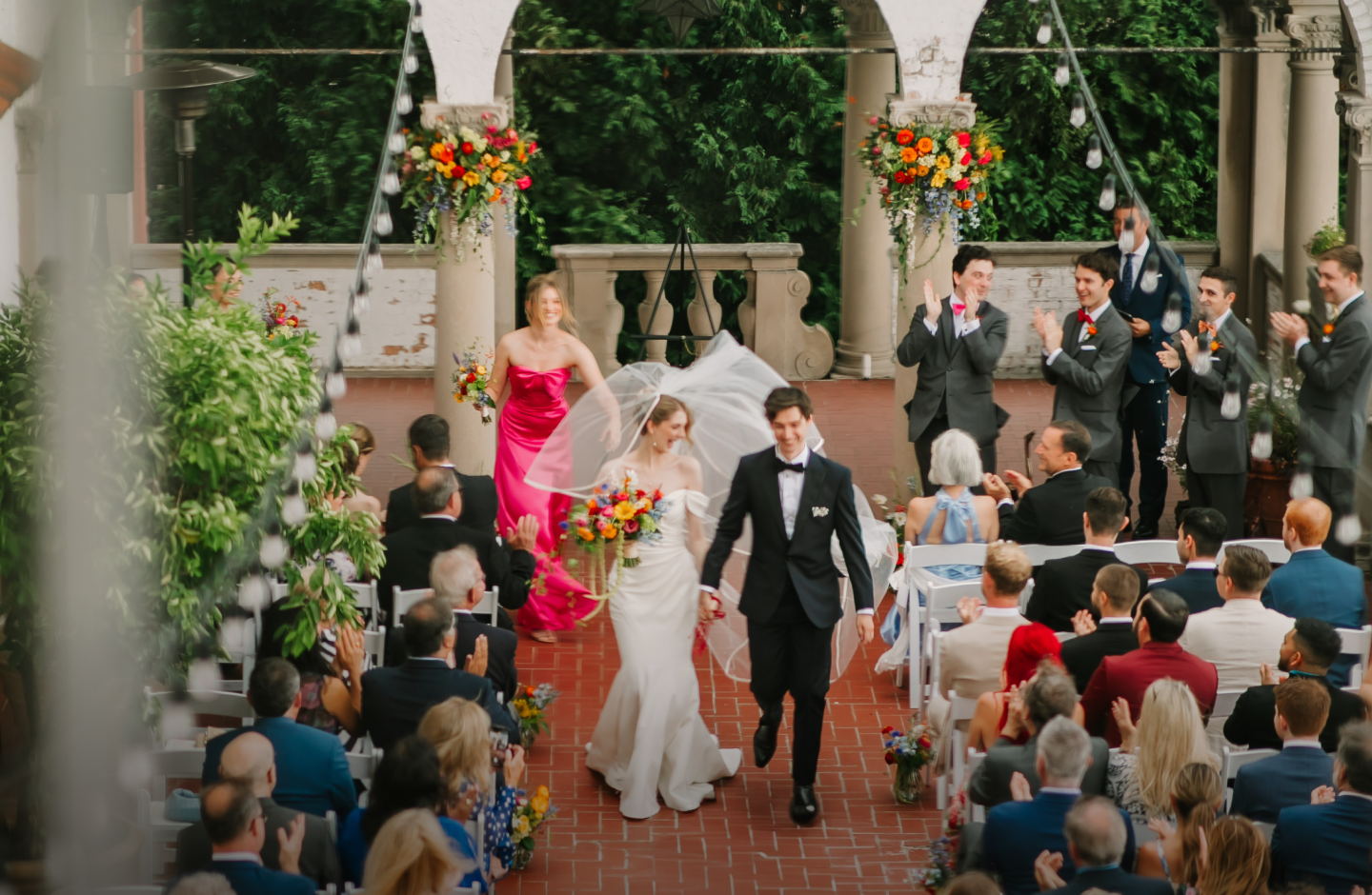 View from above of a bride and groom walking away from the altar at an outside ceremony on a terrace filled with colorful flowers.