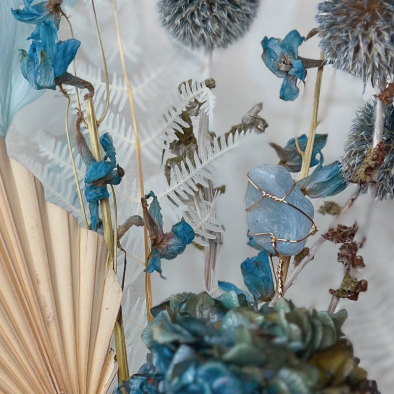 A blue lace agate crystal displayed in a blue and white dried flower bouquet
