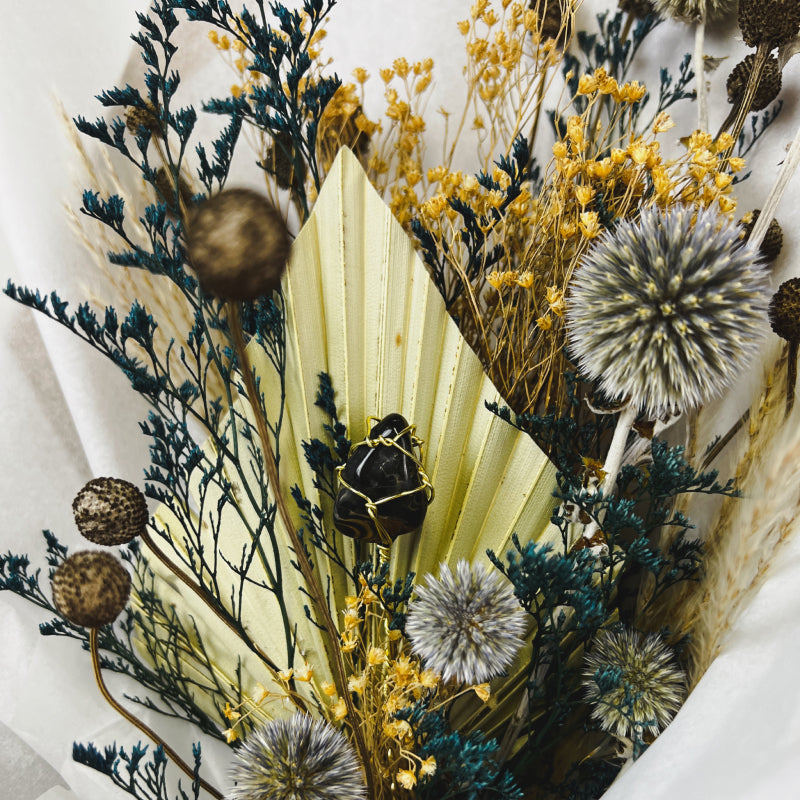 An up close shot of a brown and blue dried flower bouquet with a blue tiger's eye crystal
