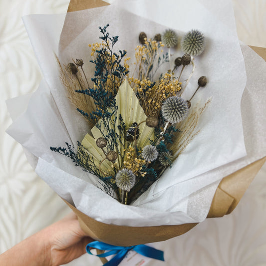 A blue and tan dried flower bouquet wrapped in paper