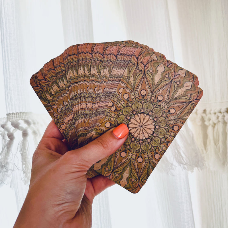 A hand holding up a splayed Botanica Oculta Tarot Deck, showing the pattern on the backs of the cards