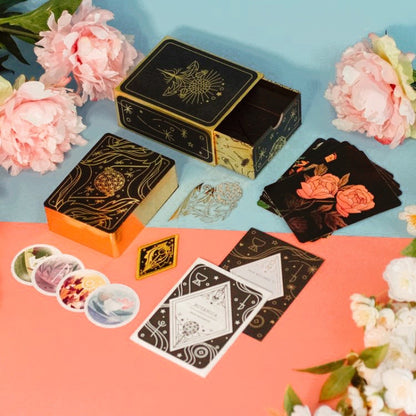 The entire contents of the Botanica tarot deck laid out on a blue and pink background with peonies laying nearby