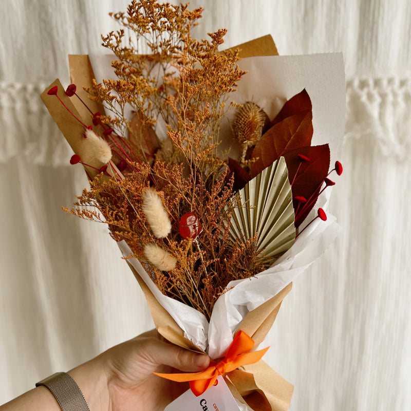 A bouquet of orange dried flowers wrapped in paper with a carnelian crystal inside