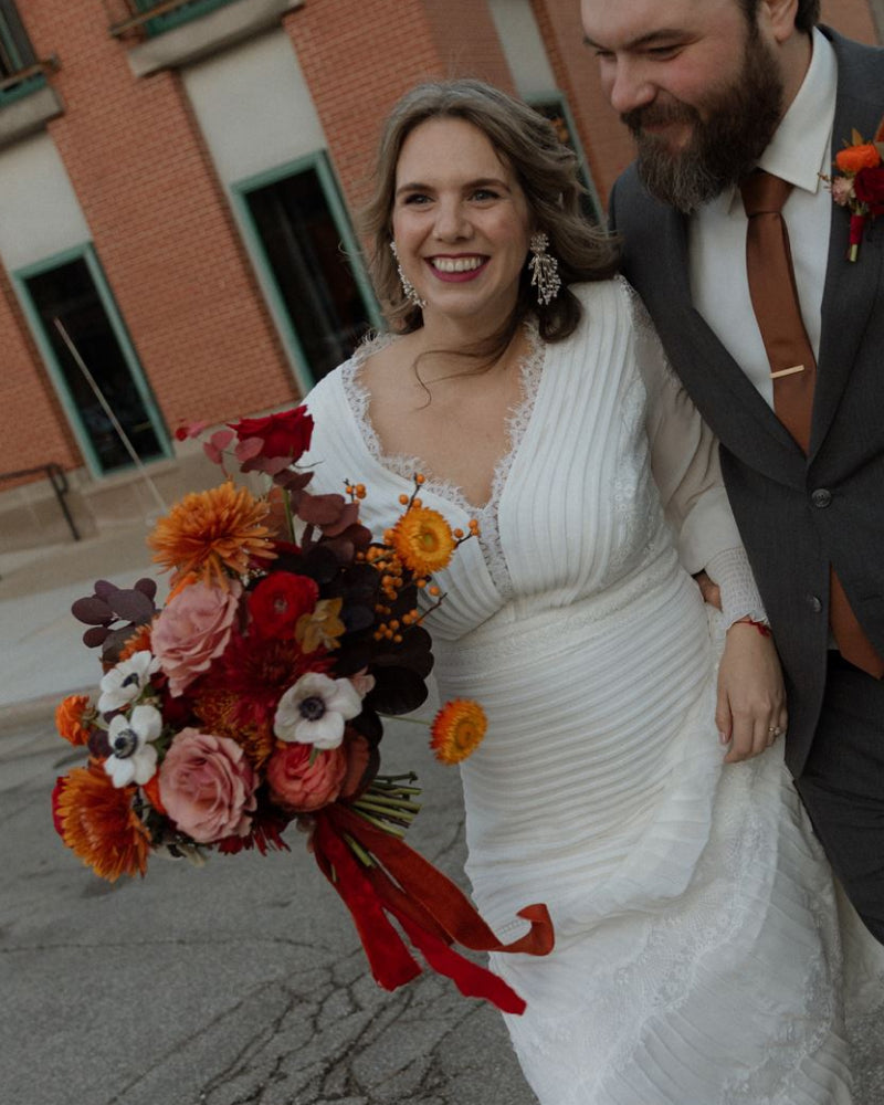 A bride holding a fall bouquet of flowers walking with her groom down a city street