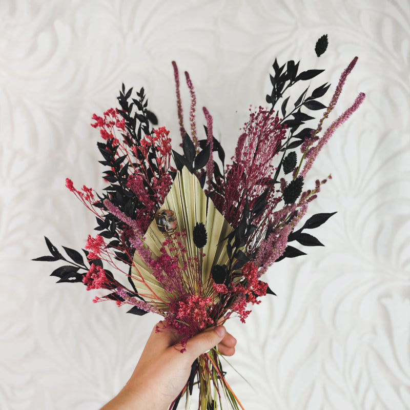 hand holding a black, pink, and tan flower bouquet with a crystal in it