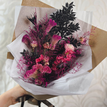 A bouquet of dried pink and black flowers with a rhodonite crystal