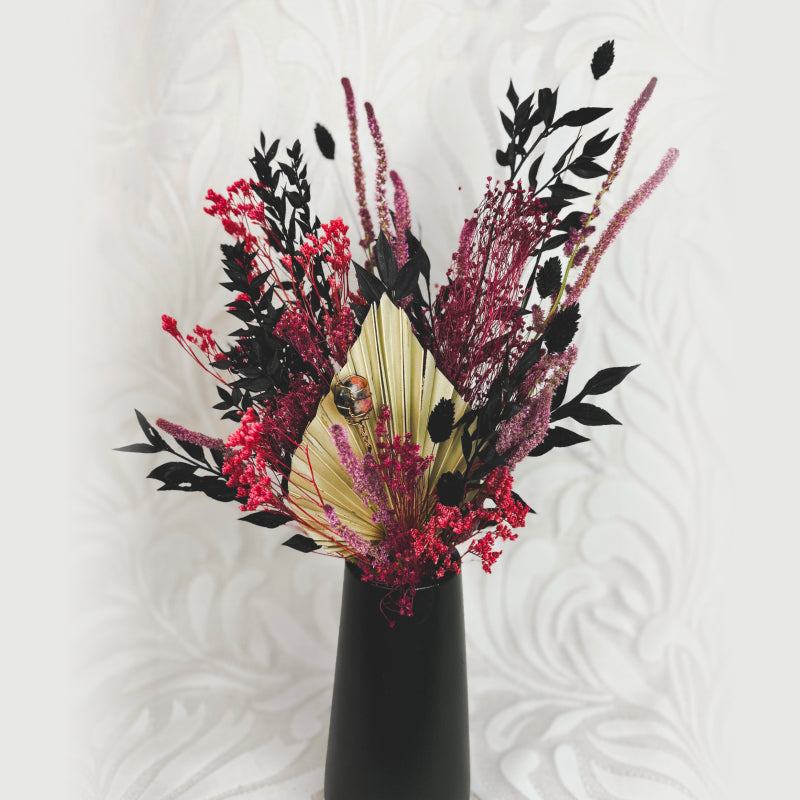 black, pink, and tan dried flower bouquet in a black vase