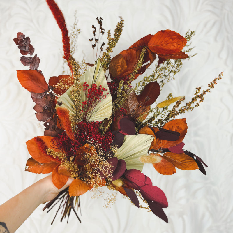 Hand holding a bouquet of orange, red, and brown dried flowers