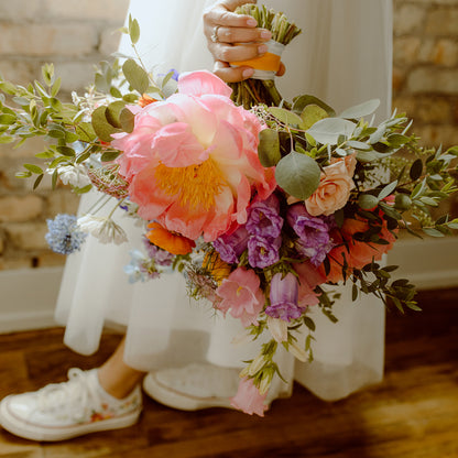 Up close shot of a bride holding a colorful bouquet down by her side, wearing floral embroidered converse sneakers