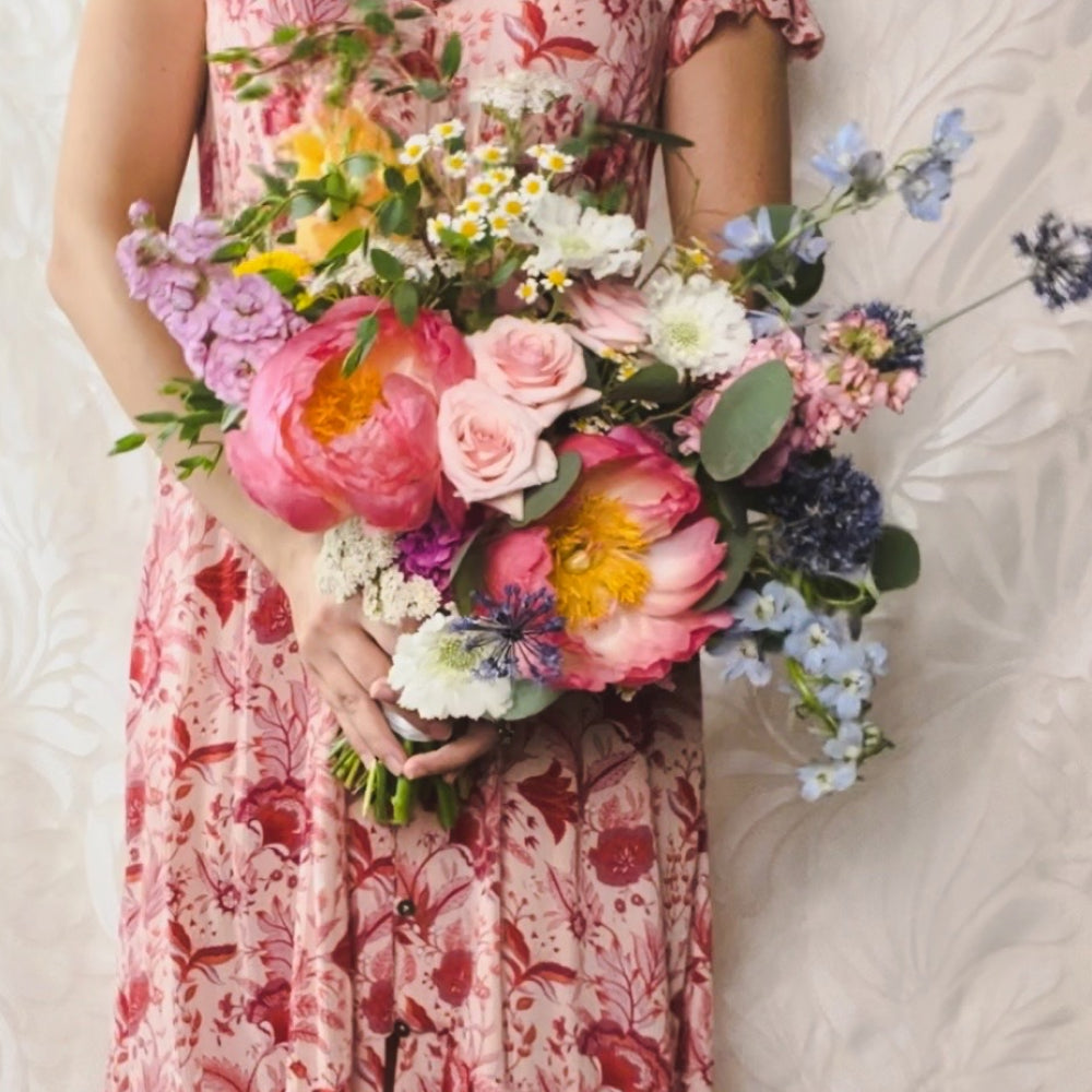A woman from the shoulders down in a pink floral-patterned dress holding a colorful bouquet of flowers
