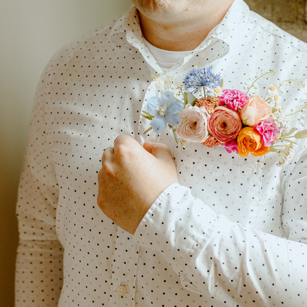 A groom in a dress shirt showing off the colorful pocket square boutonniere in his pocket