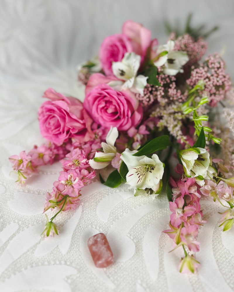 A bouquet of pink flowers laying on its side with a strawberry calcite crystal next to it