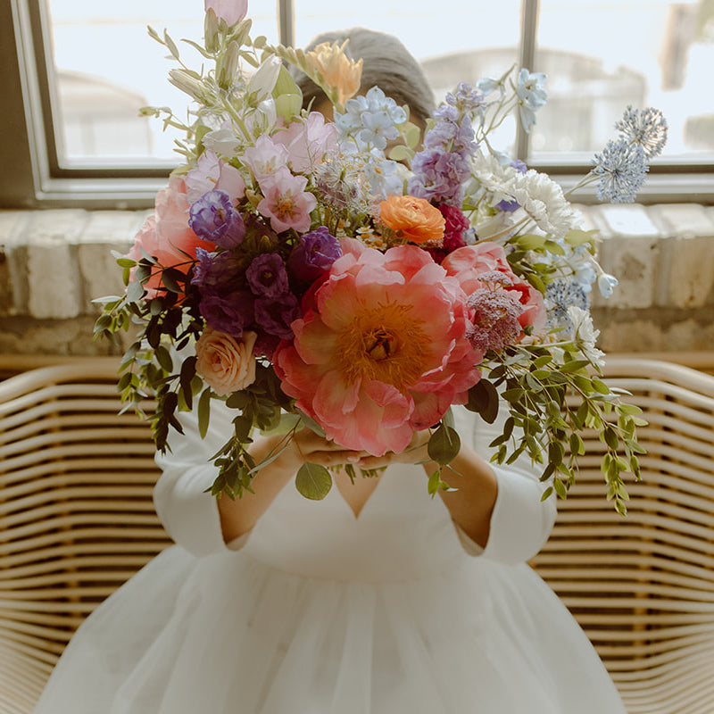 A bride holding a colorful bouquet up over her face