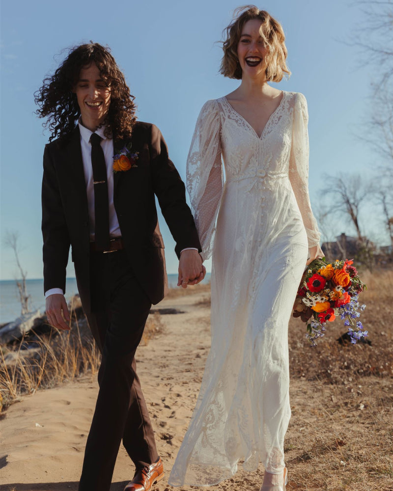 A bride and groom walking along the beach holding hands smiling