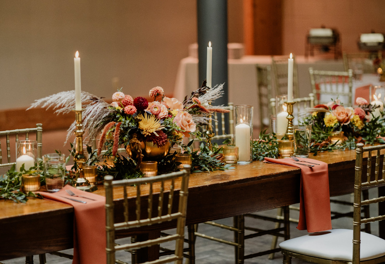 A long wooden table set with cream candles in brass holders with floral centerpieces