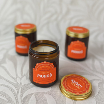 Three candles in brown glass with an orange label that reads "Mokoś"