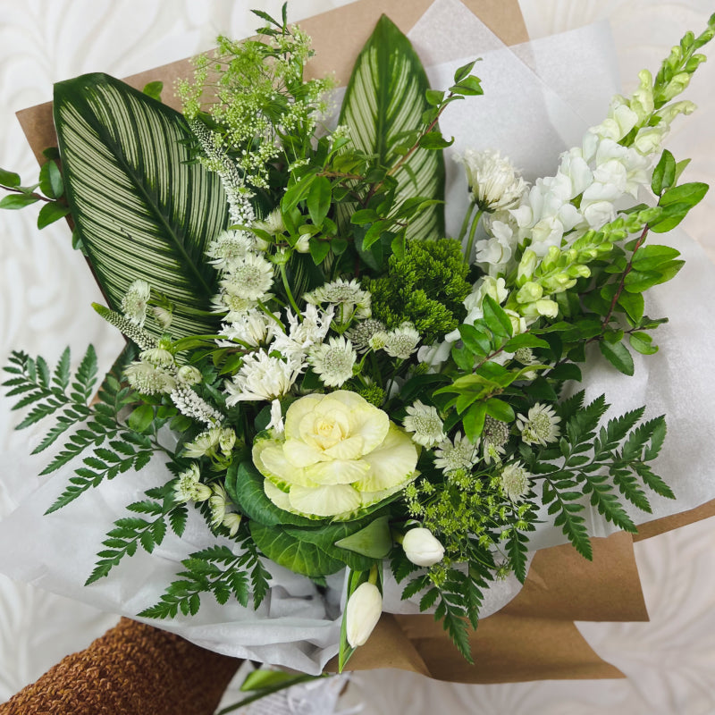 A wrapped flower bouquet filled with interesting greenery and white textural flowers