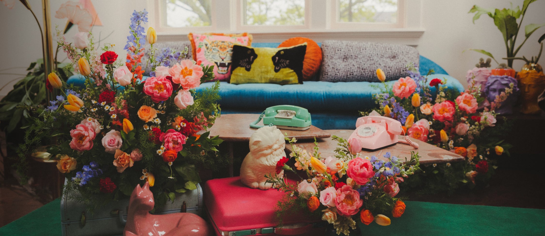 A room featuring multiple large, colorful floral arrangements and vintage decor, including pastel phones