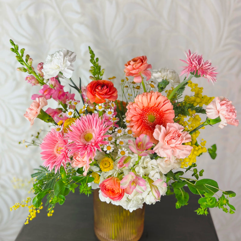 A large vase arrangement filled with bright pink, yellow, white, and peach flowers