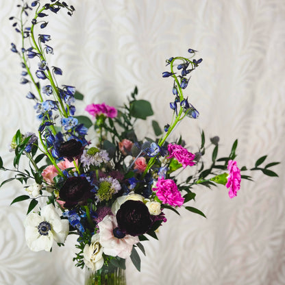 Dark purple, blue, bright pink, white, and lavender flowers in a clear vase