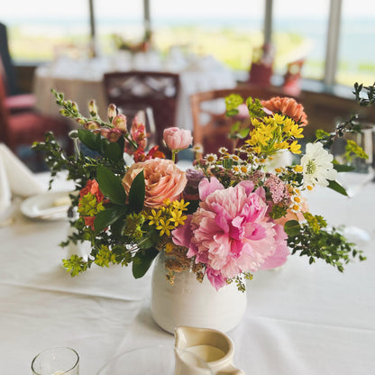A white vase filled with a variety of fresh flowers on a table in an event space