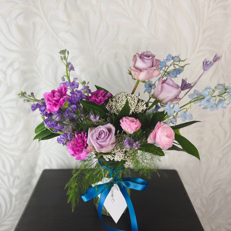 A vase arrangement with purple, pink, and blue flowers