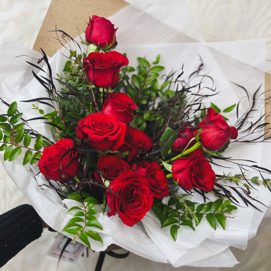 A wrapped bouquet of a dozen red roses and greenery