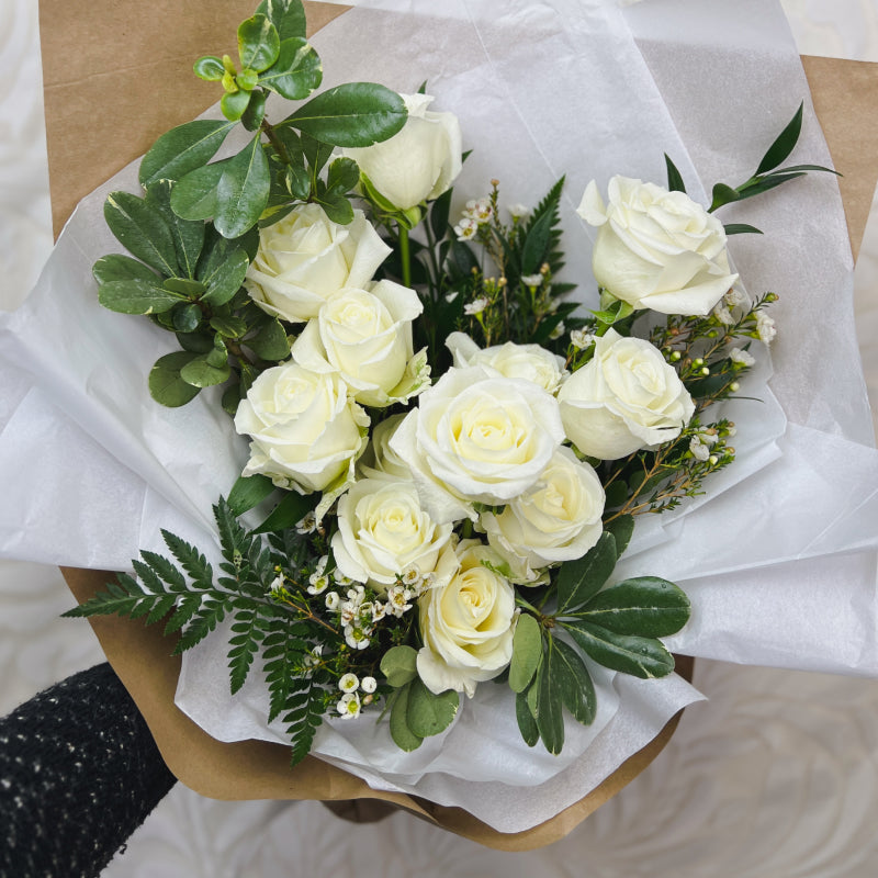 A dozen white roses with pretty greens and small white flowers wrapped in paper