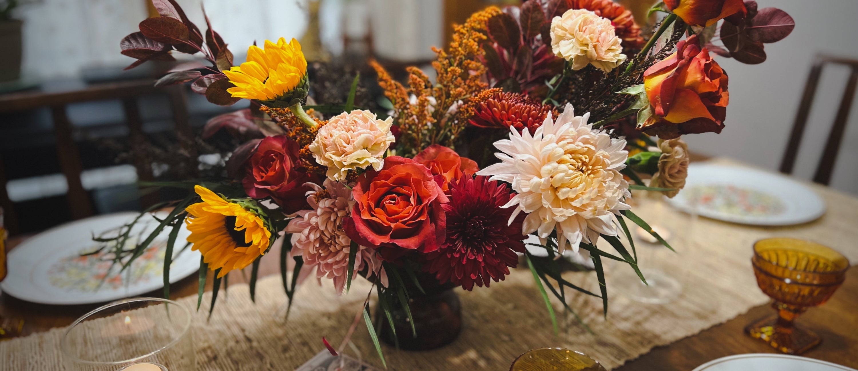 A premium centerpiece of fall flowers in an amber glass vase on a table set for thanksgiving