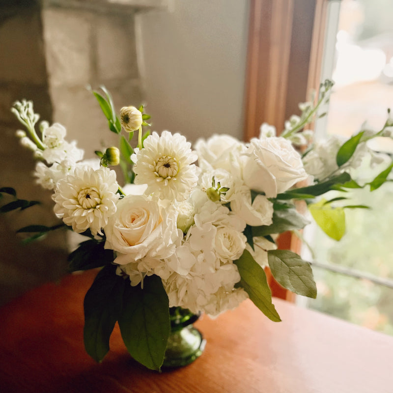 A small vintage green glass compote vase filled with white flowers and greens