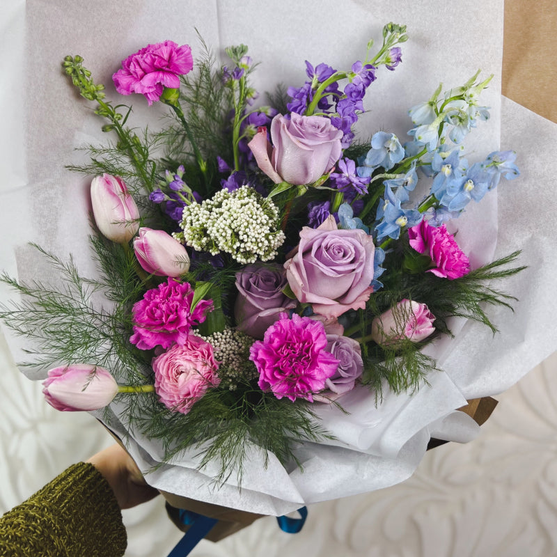 A wrapped bouquet of bright pink, bright purple, lavender, and light blue flowers