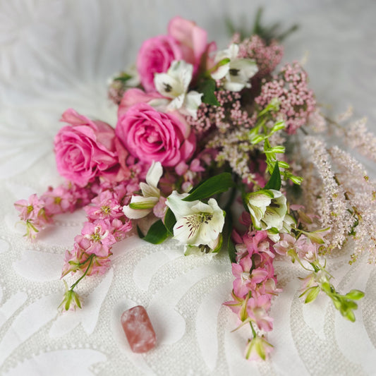 A pretty pink and white flower bouquet lying on its side, next to a Strawberry Calcite crystal