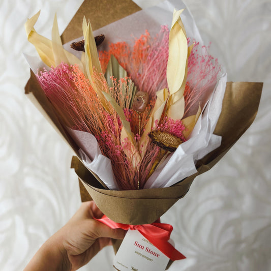 A wrapped bouquet featuring dried flowers in peach, pink, and white