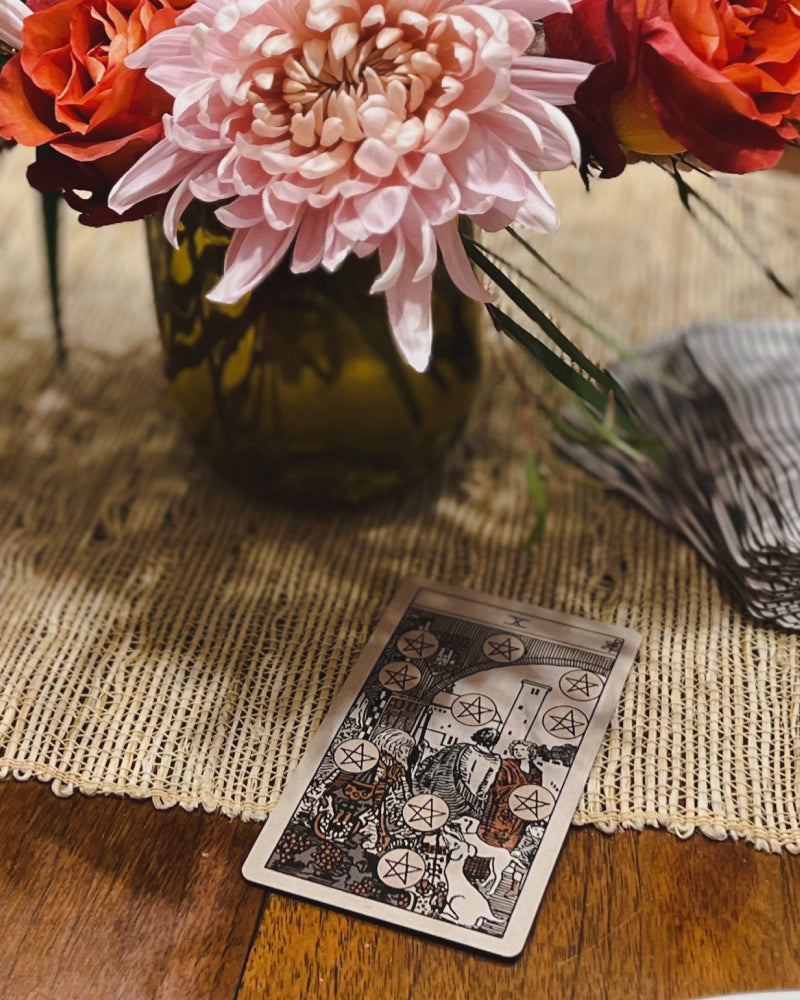 The ten of pentacles tarot card on a table next to a vase of flowers