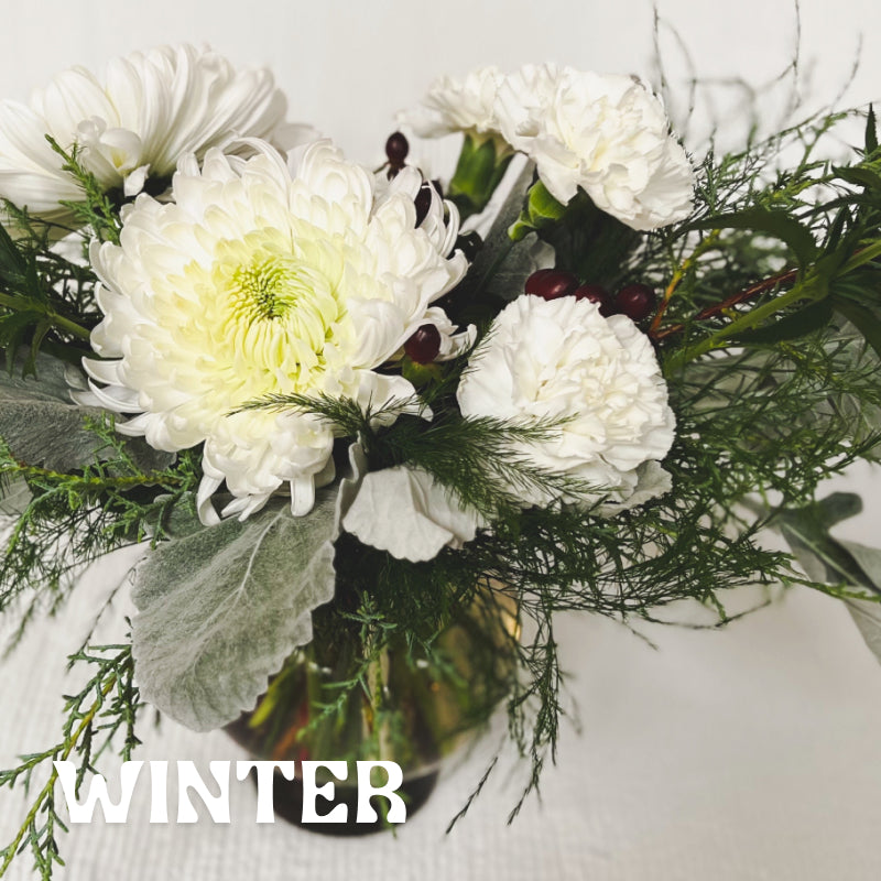 Seasonal winter vase arrangement with evergreens, red berries, and white flowers