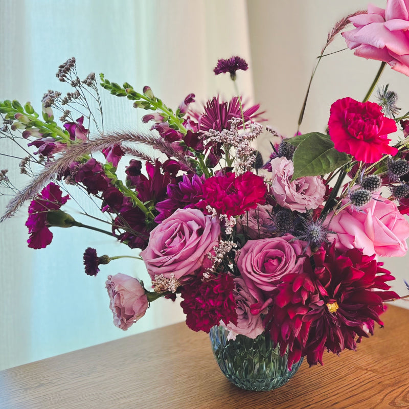 Deluxe vase arrangement in an enchanting color palette of dark purples, magentas, and blues, featuring roses, dahlias, and more