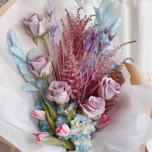 Wrapped bouquet of pastel flowers, fresh and dried, in light pinks, blues, and lavenders 