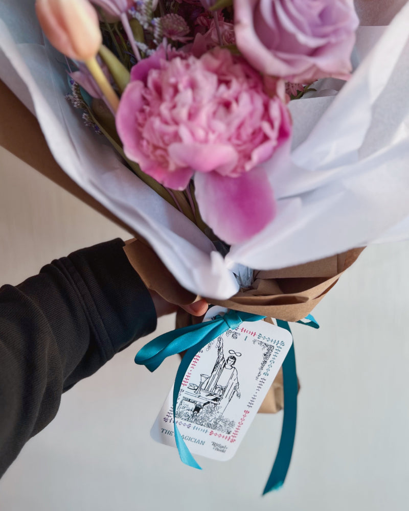 A wrapped bouquet of flowers with a The Magician tarot card tied to it with ribbon