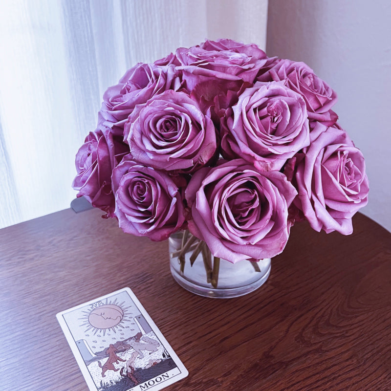 A small domed arrangement of purple roses with a The Moon tarot card