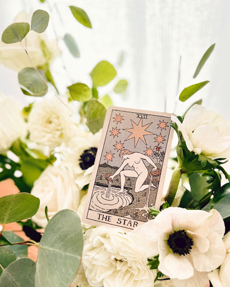 The Star tarot card propped against white flowers