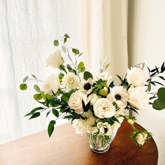 A large assortment of premium white flowers and greenery in a clear white vase
