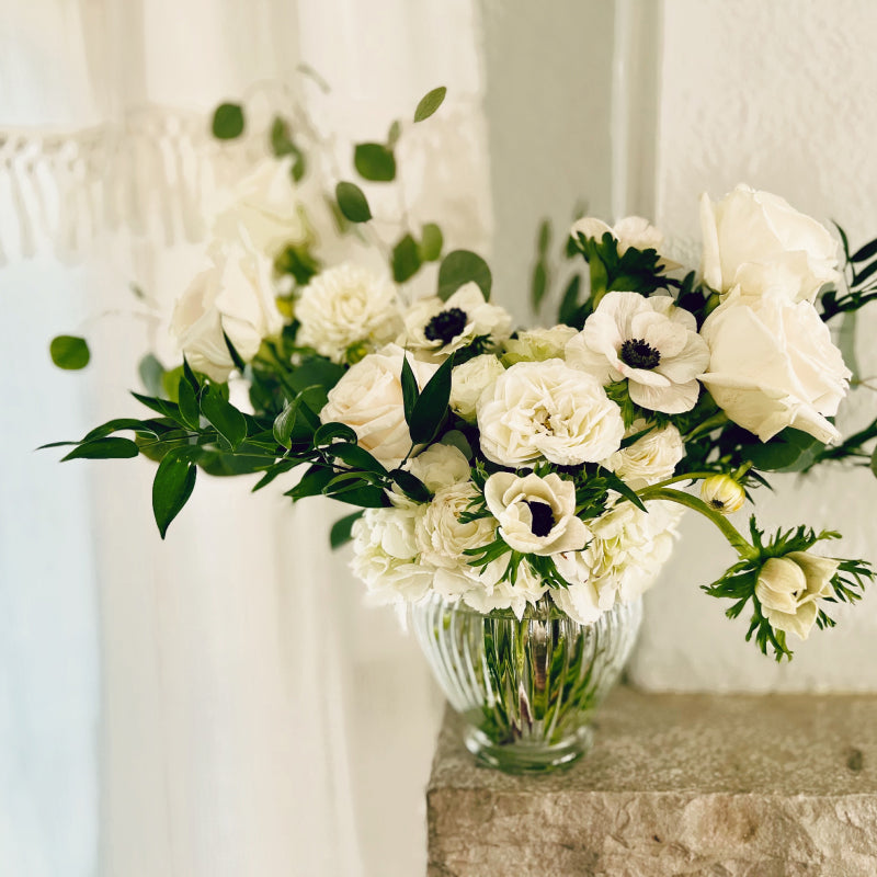 A large arrangement of white flowers and greenery sitting atop a fireplace mantel 