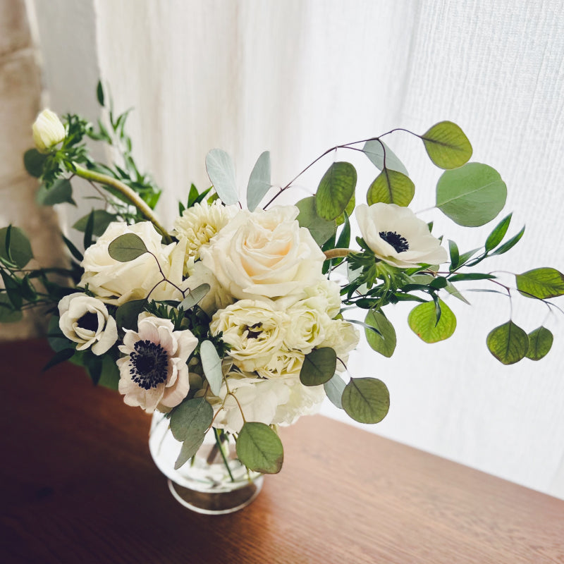 A small arrangement of white flowers and greenery in a clear glass vase