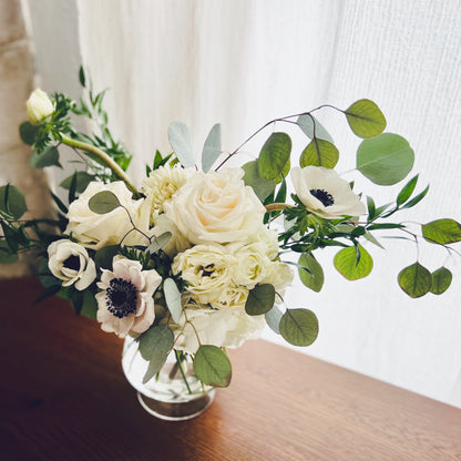 A small arrangement of white flowers and greenery in a clear glass vase