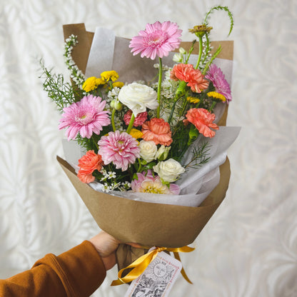 Cheerful wrapped bouquet of pink, yellow, and white flowers with a The Sun tarot card attached